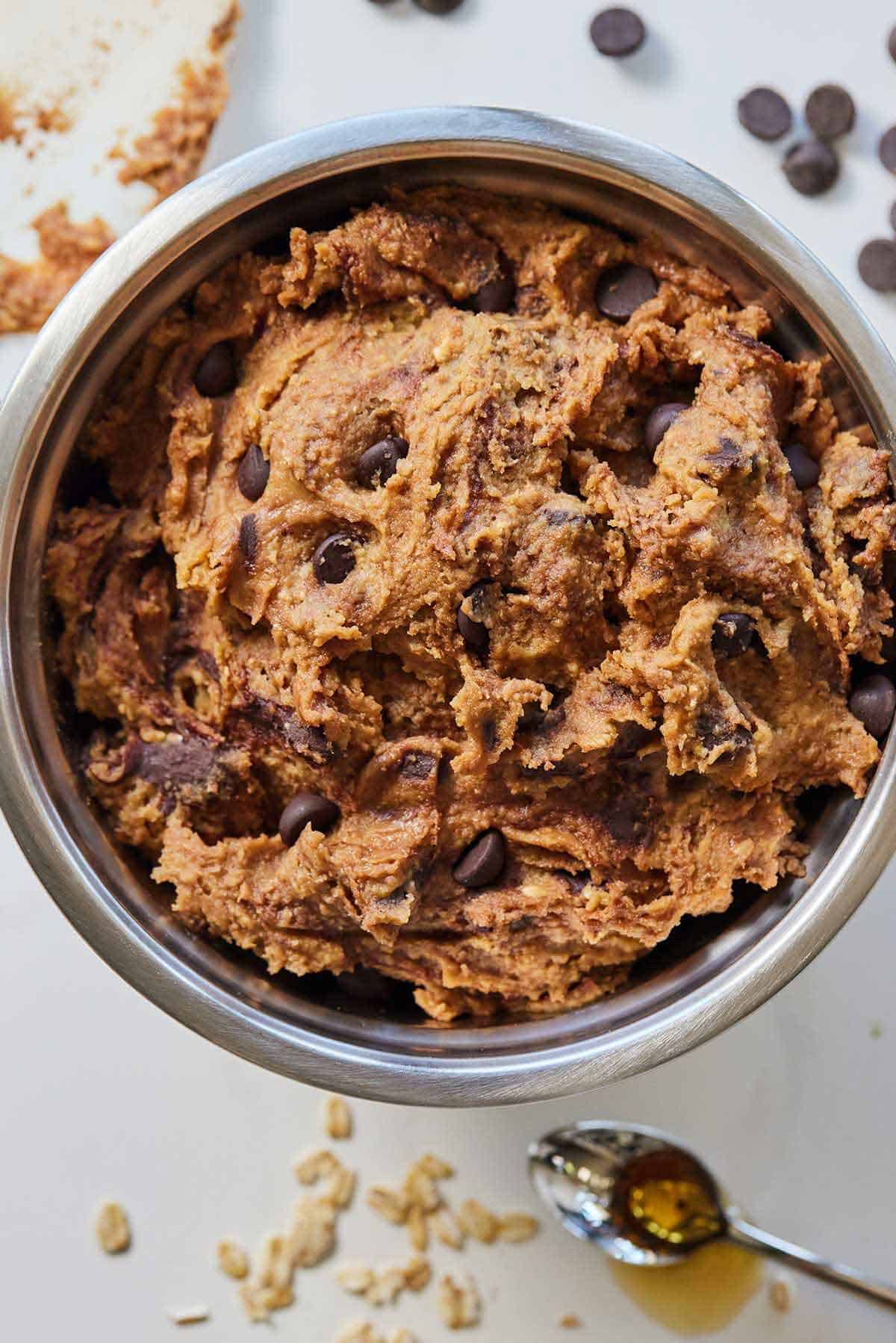 Overhead view of a bowl of chickpea cookie dough on a countertop with ingredients scattered around it.