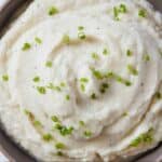 Pinterest graphic of a bowl of mashed cauliflower with chives on top.