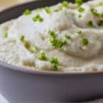 Pinterest graphic of a profile view of a bowl of mashed cauliflower with chives on top.