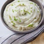 Pinterest graphic of a bowl of mashed cauliflower beside a linen napkin and wooden spoon.