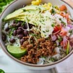 Pinterest graphic of a taco bowl with a lime wedge, sliced avocado, black beans, pic de gallo, corn, and shredded cheese by the ground beef.