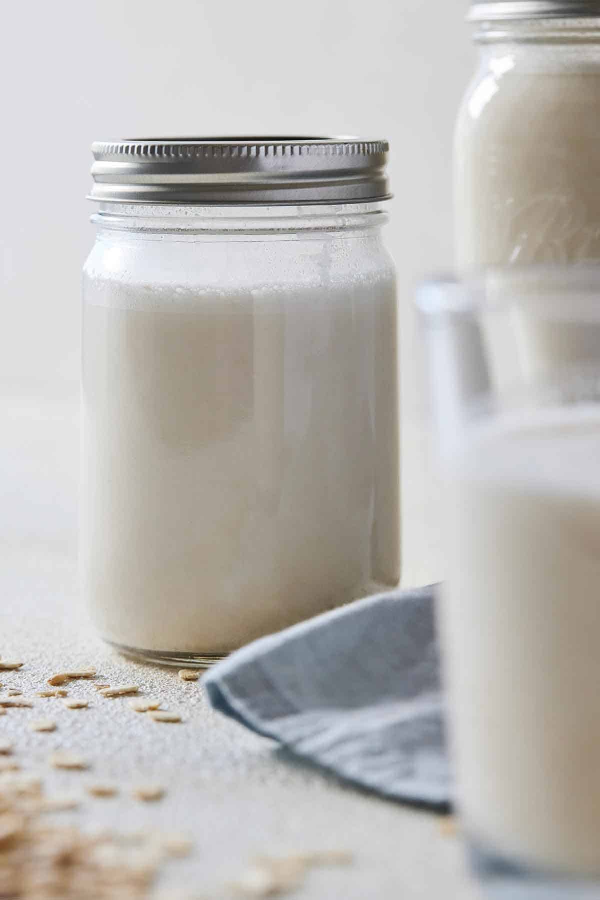 Oat milk in a mason jar with a cup in front, out of focus.