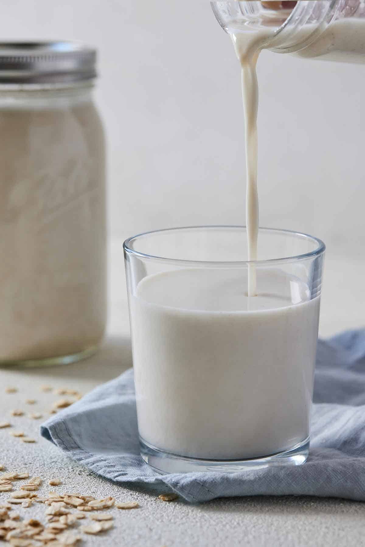 A glass with oat milk poured in it with a full mason jar of oat milk in the background.