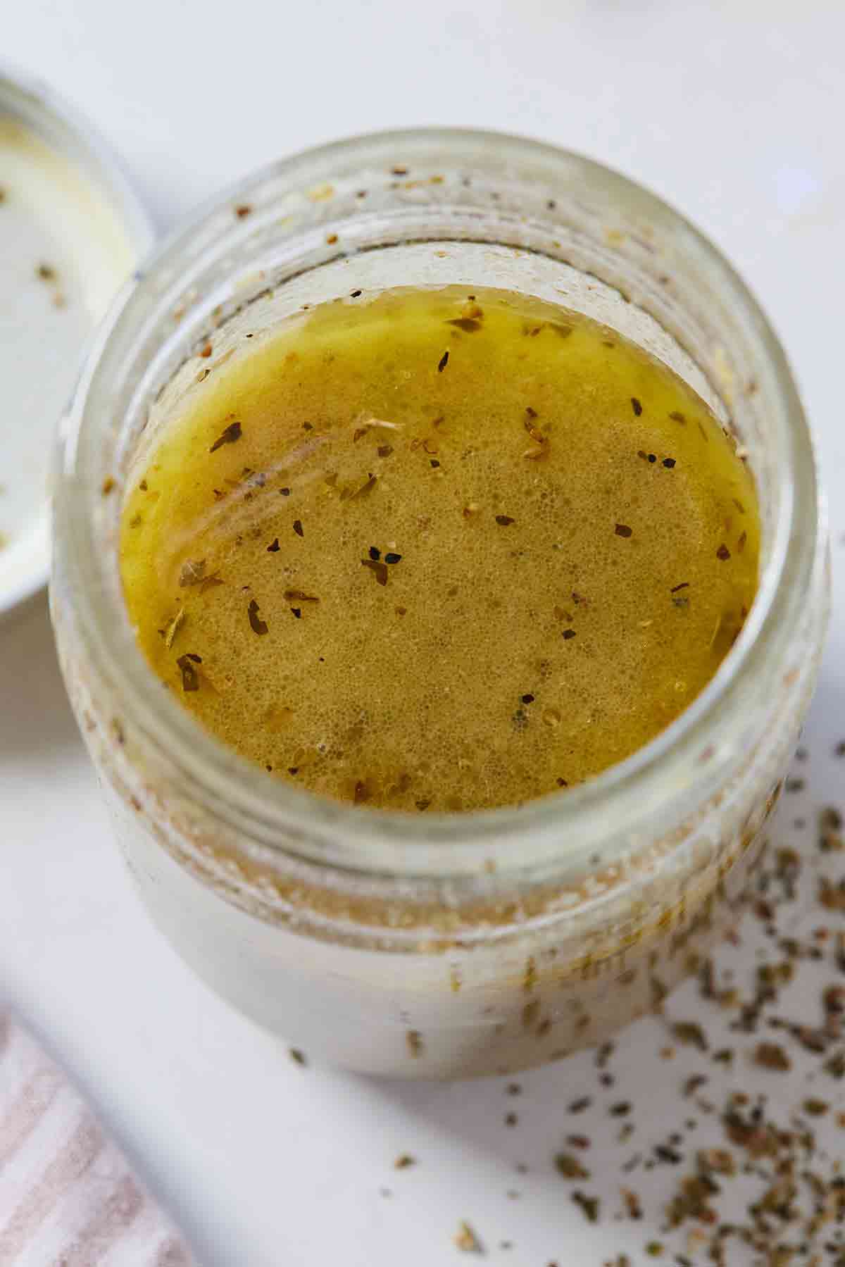 Overhead view of a mason jar of red wine vinaigrette with oregano sprinkled around the counter.