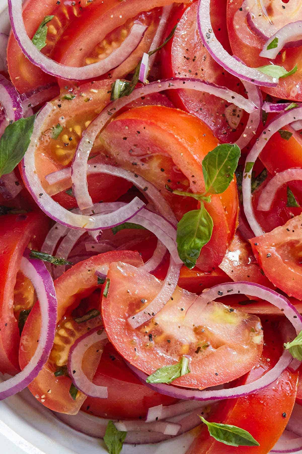 Close up of cut tomatoes, sliced onions, and fresh basil.