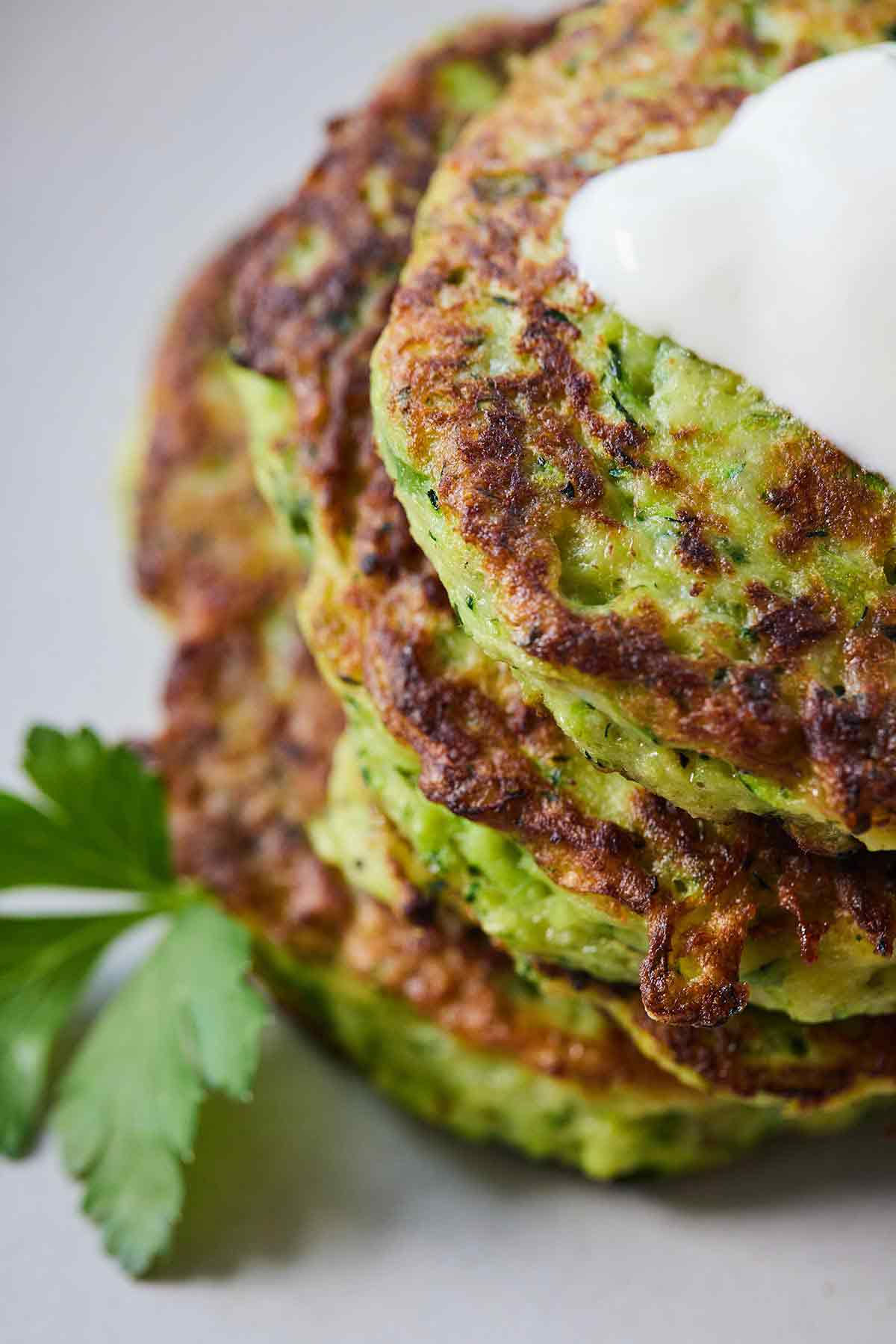 Close up view of zucchini fritters with a spoonful of sour cream on top and a piece of parsley on the side.