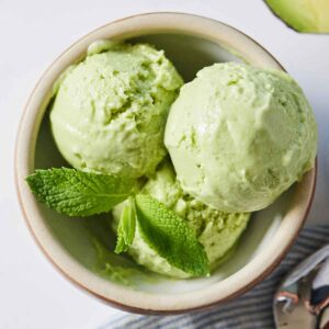 Overhead view of three scoops of avocado ice cream with fresh mint on top.