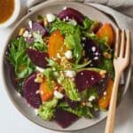 Close up of a plate of beet salad with greens and cheese with a wooden fork.