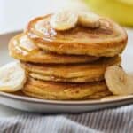 A plate of four paleo pancakes with sliced bananas.