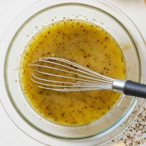 Overhead close up of a glass bowl of red wine vinaigrette with a metal whisk inside.