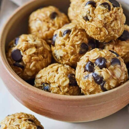 A bowl of multiple energy balls with a single one out on the counter.