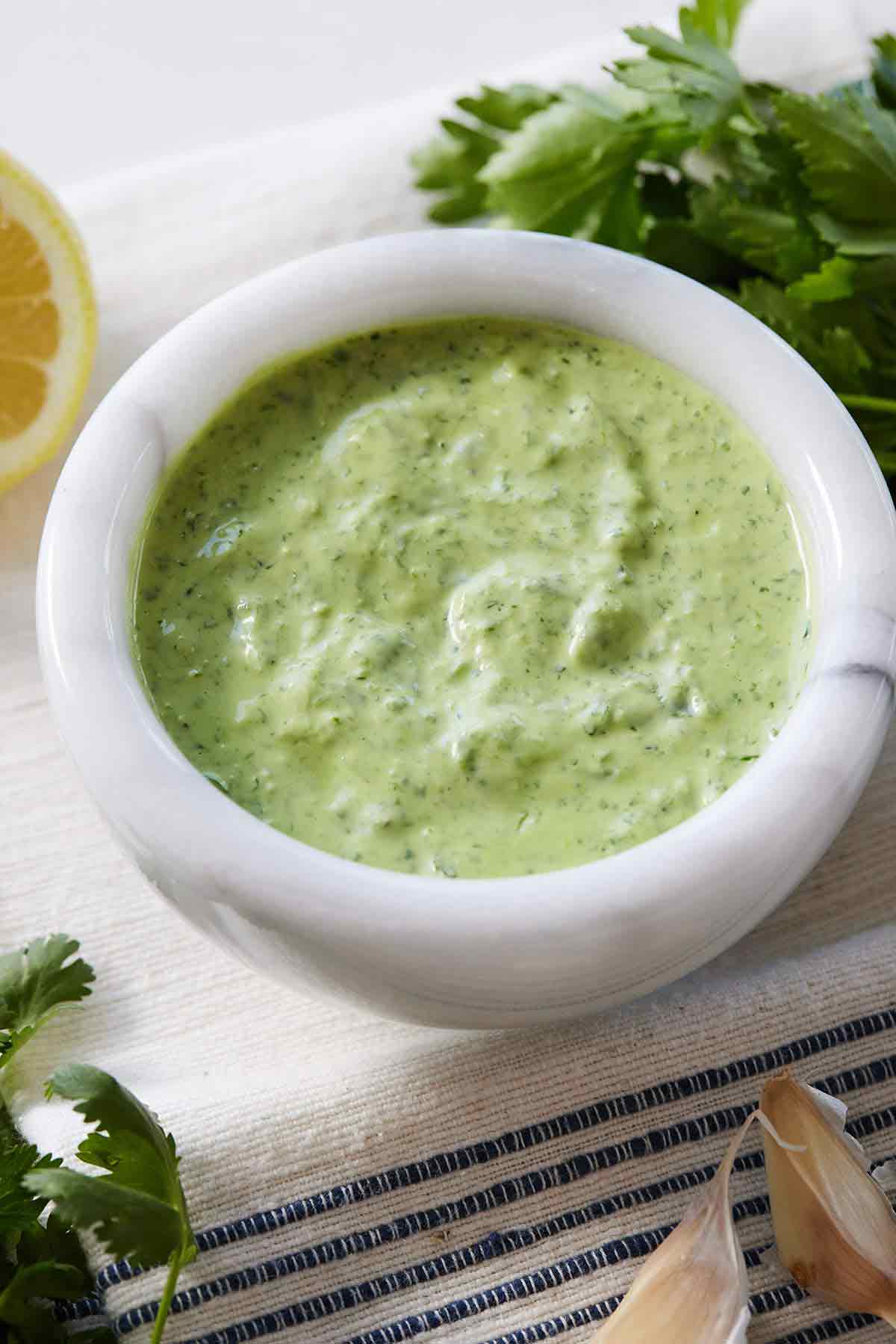 Green goddess dressing with fresh herbs and garlic cloves around it.