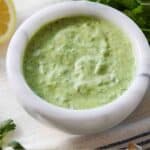 Pinterest graphic of a bowl of green goddess dressing with some fresh herbs around it.