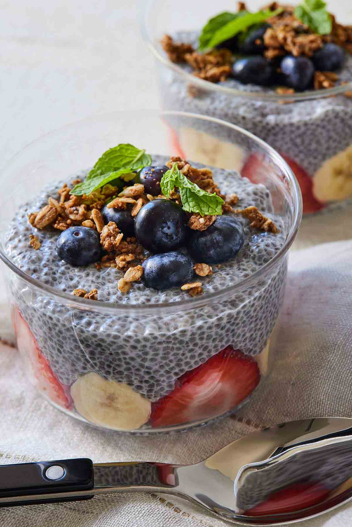 Two small bowls of chia pudding with granola and fresh fruit. A spoon is lying in the front.