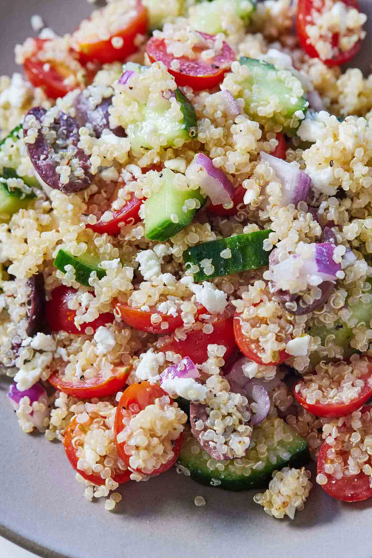 Close up image of a Greek quinoa salad with red onions, cucumbers, tomatoes, and olives.
