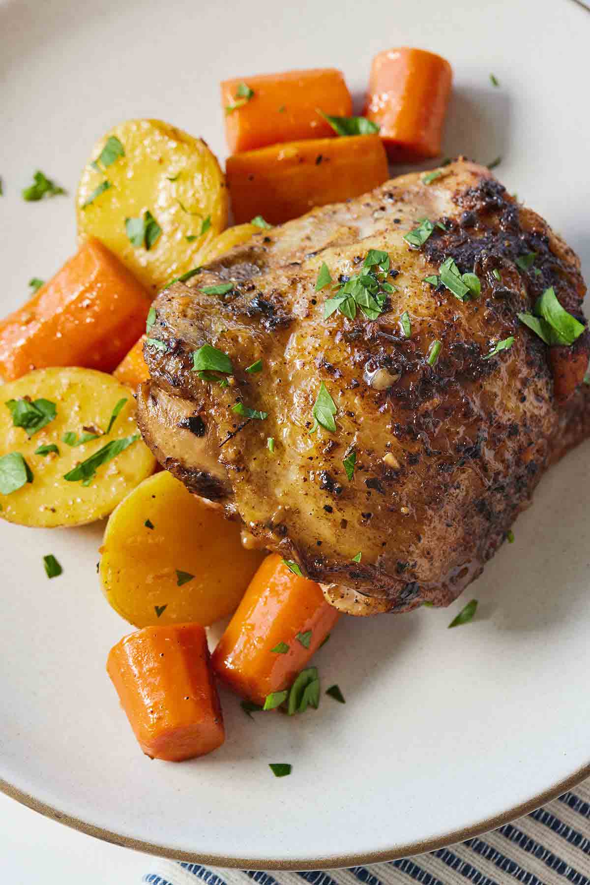 A plate with balsamic chicken thigh with carrots and potatoes.