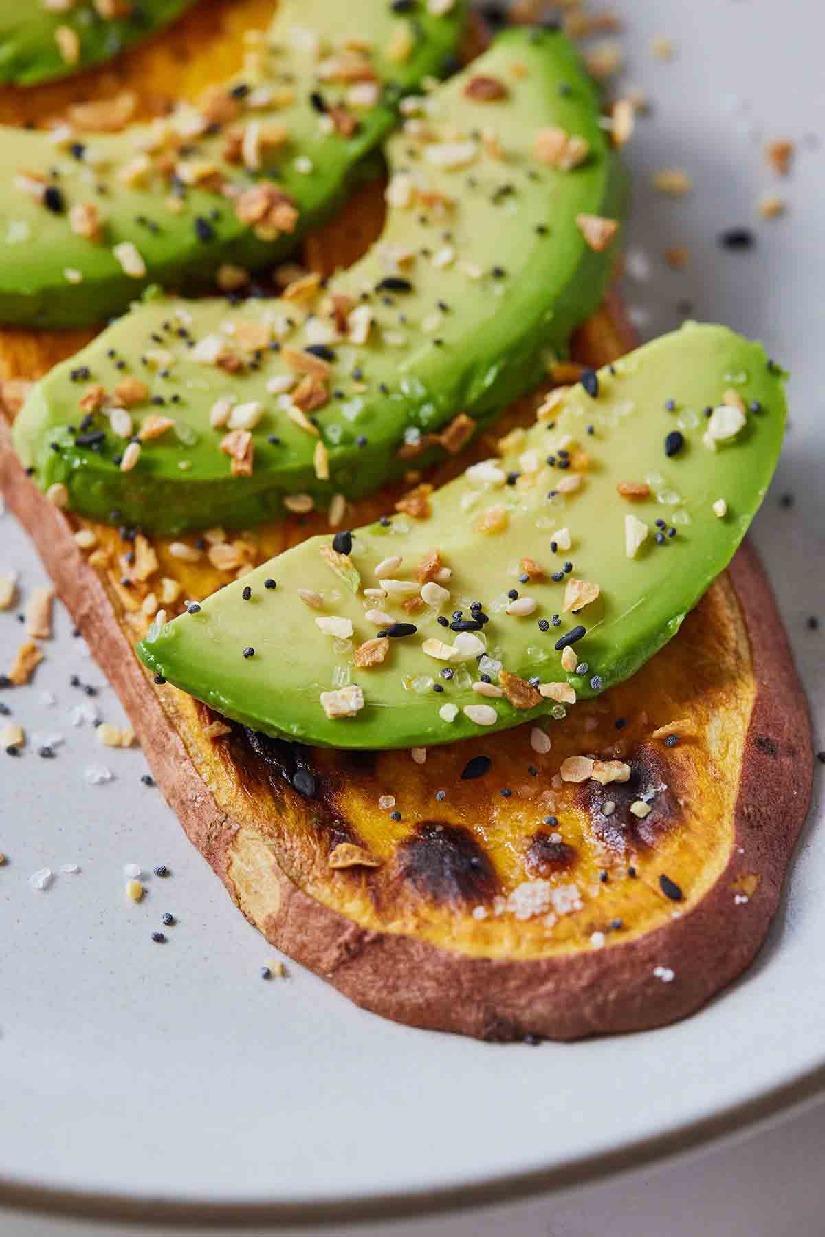 Close up of a slice of sweet potato toast with sliced avocado and everything bagel seasoning sprinkled on top.