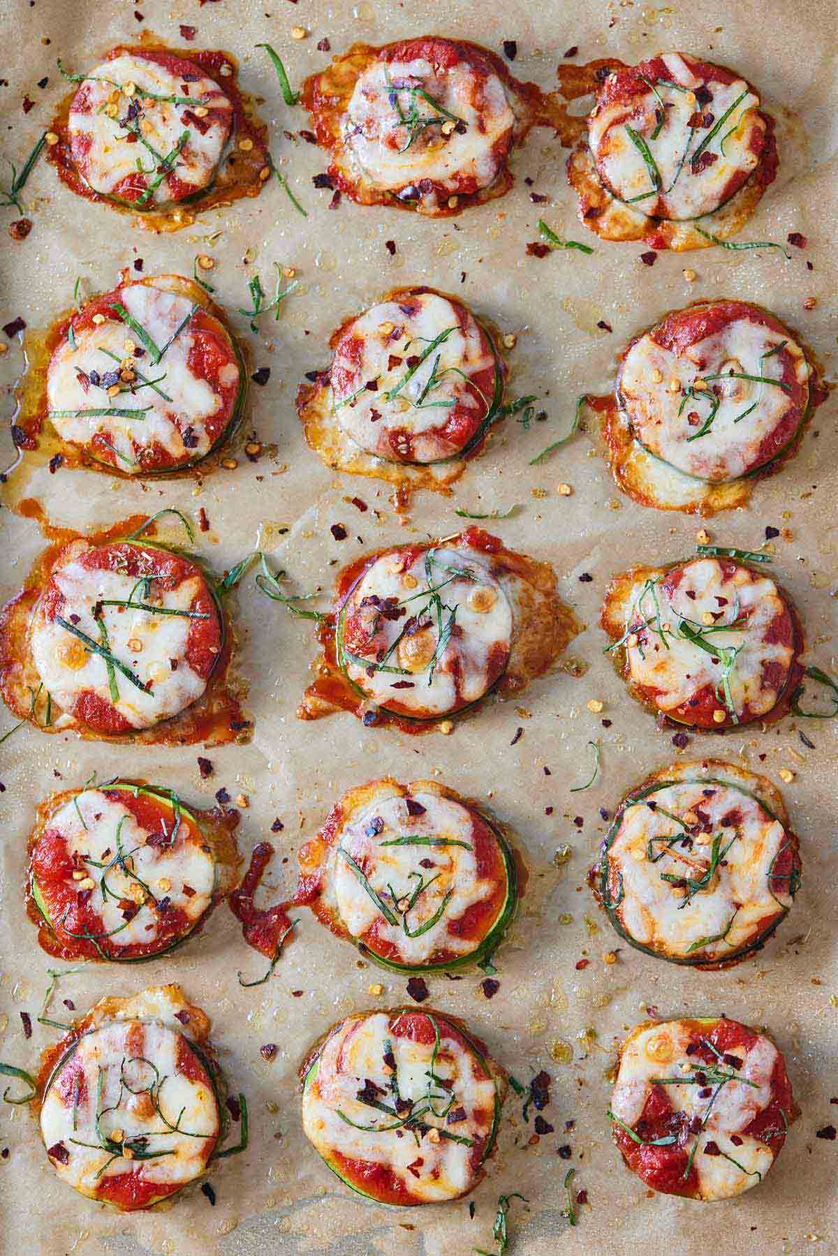 Overhead view of 15 zucchini pizza bites on a parchment lined sheet pan.