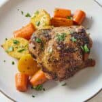 Overhead view of a plate with a chicken thigh with potatoes and carrots.