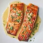 Overhead view of two pan seared salmon fillets with a butter sauce on top.