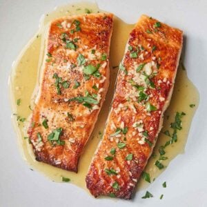 Overhead view of two pan seared salmon fillets with a butter sauce on top.