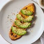 Overhead view of a plate with a sweet potato toast with avocado slices on top.