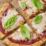 Pinterest graphic of a cauliflower pizza cut into four slices with basil leaves on top.