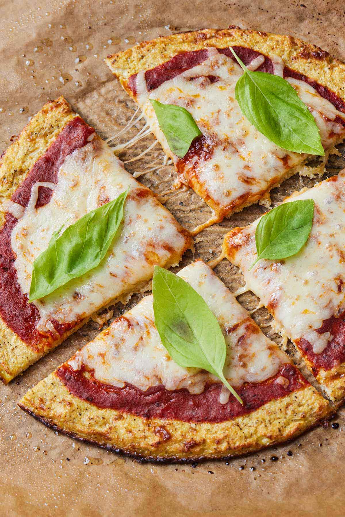A cauliflower pizza crust topped with sauce, cheese, and basil, cut into four slices.