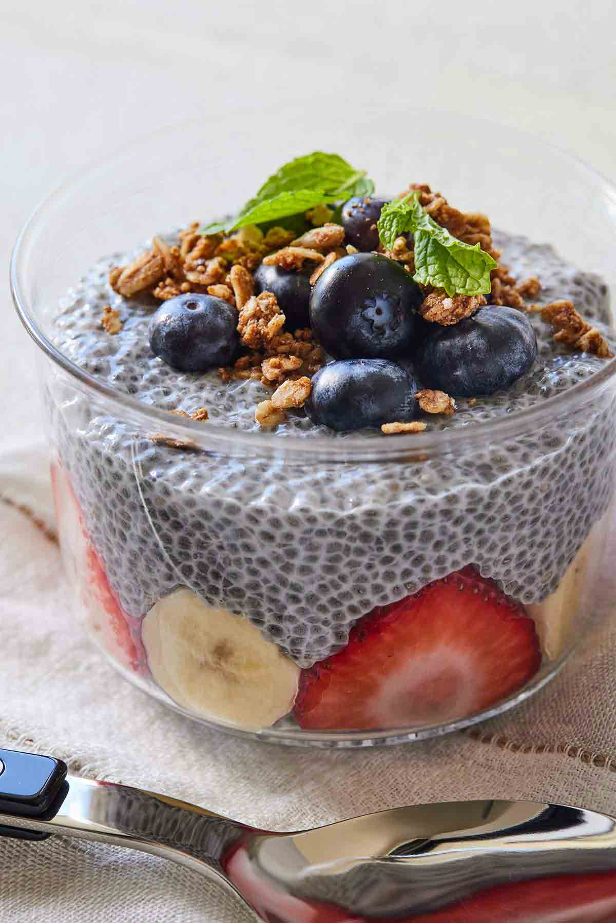 A small bowl of chia pudding with strawberries and banana slices inside and blueberries, granola, and mint on top.