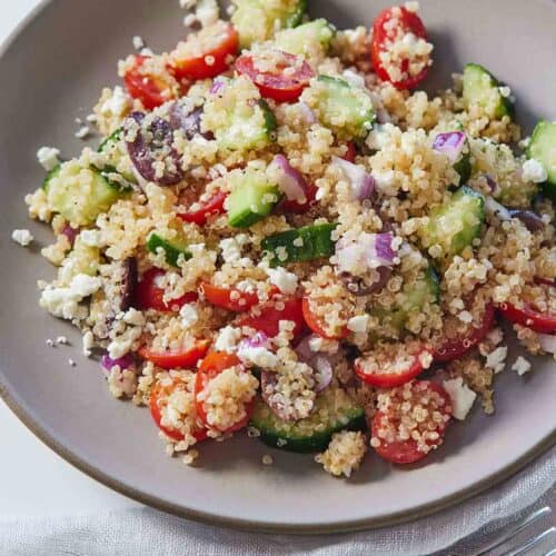 A plate of Greek quinoa salad with a fork beside the plate.