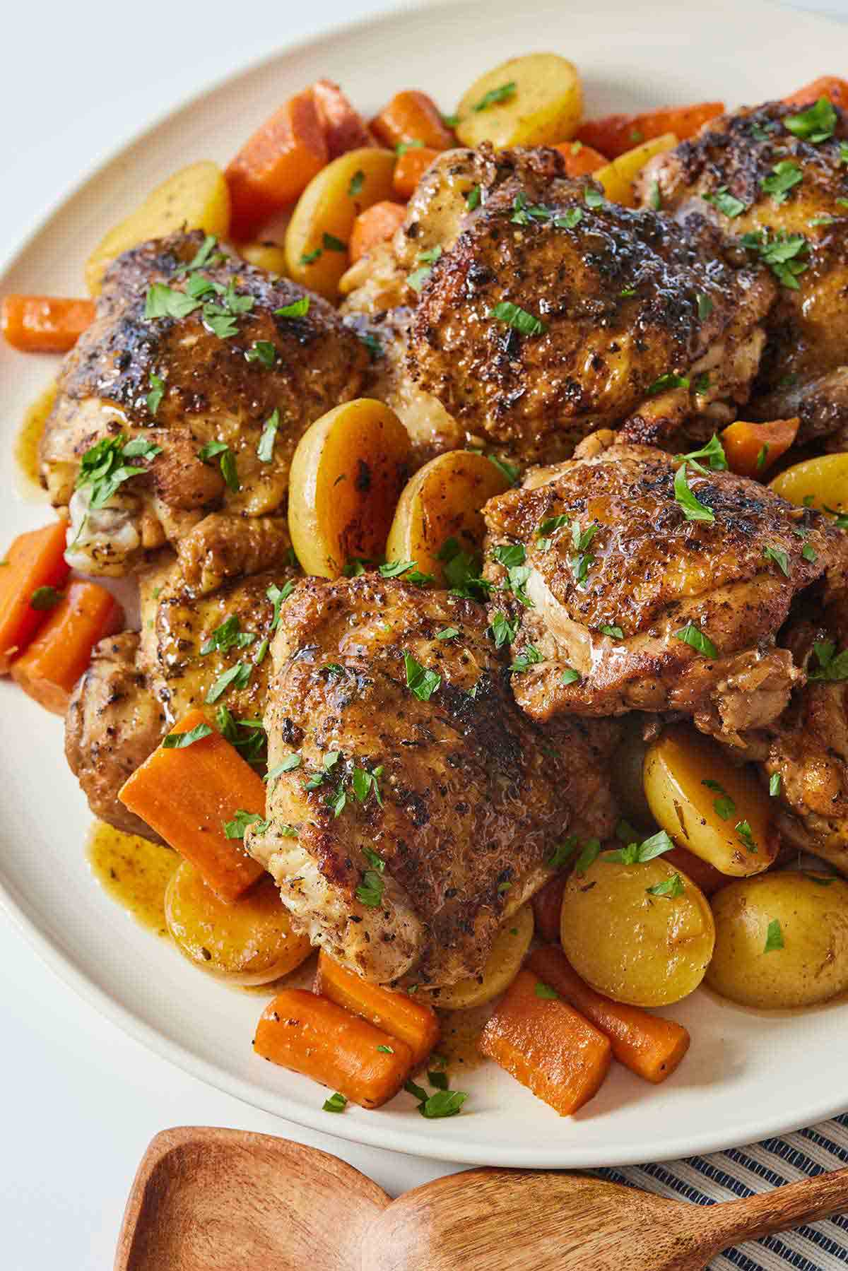 A platter of balsamic chicken thighs over top a bed of carrots and potatoes.