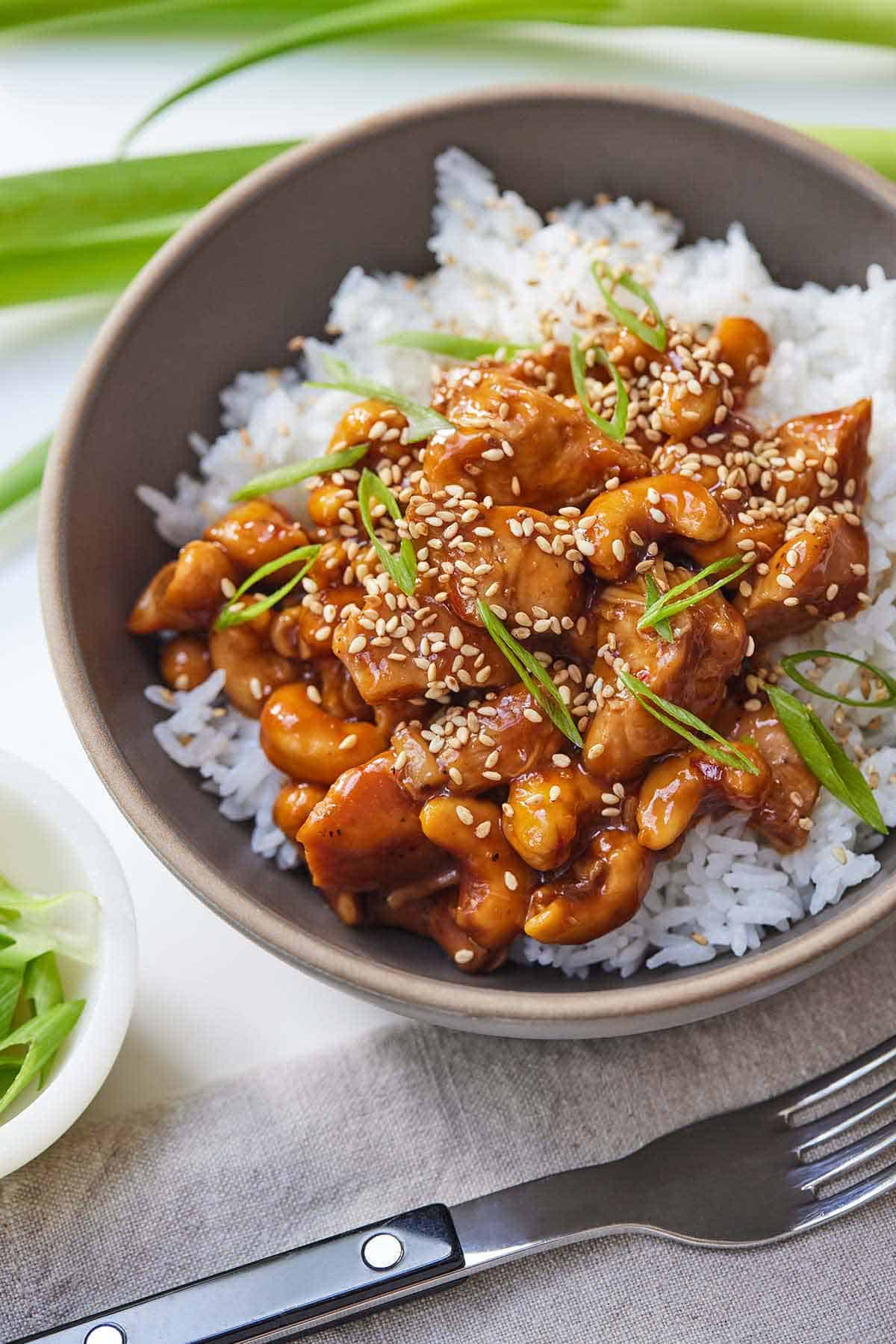 A bowl of rice with cashew chicken with green onion and sesame seeds as garnish.
