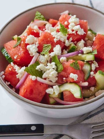 A bowl of watermelon salad with a fork in front.