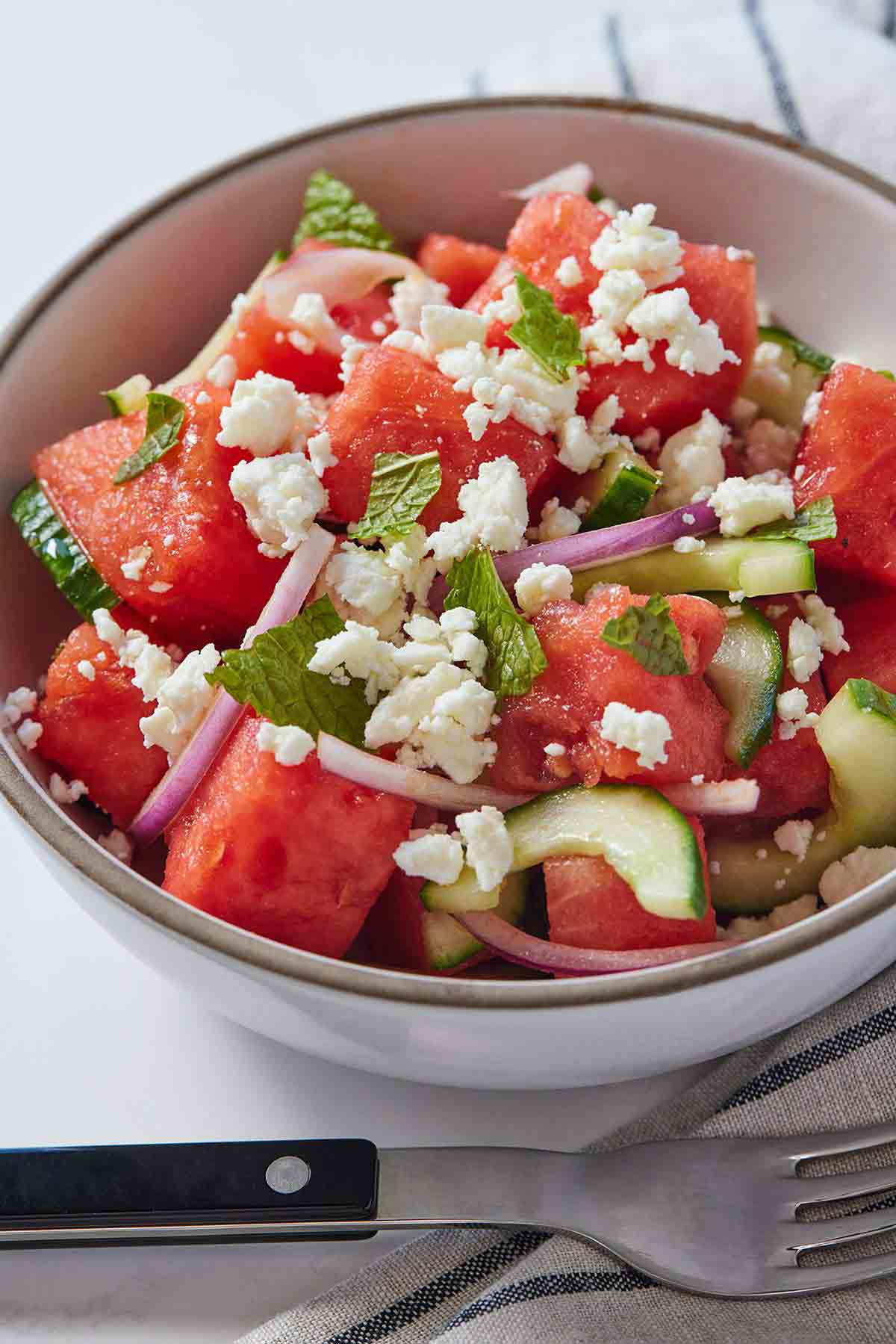 A bowl of watermelon salad with a fork in front.