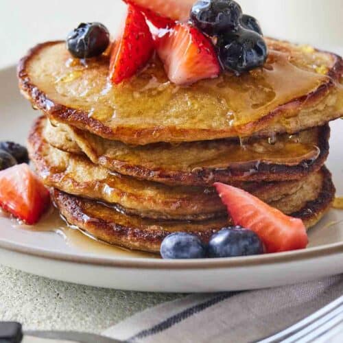 A stack of multiple banana oatmeal pancakes with fruit on top.