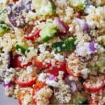 Pinterest graphic of a close up view of a Greek quinoa salad showing fresh vegetables tossed with quinoa.