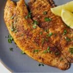 Pinterest graphic of the overhead view of a piece of pan fried tilapia with two lemon wedges beside it.