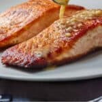 Pinterest graphic of butter sauce being spooned over the top of two pan seared salmons.