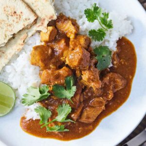 Overhead view of a plate of Instant Pot chicken tikka masala with some rice, cilantro, and naan.