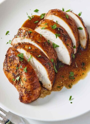 A white plate with a balsamic chicken breast, sliced.