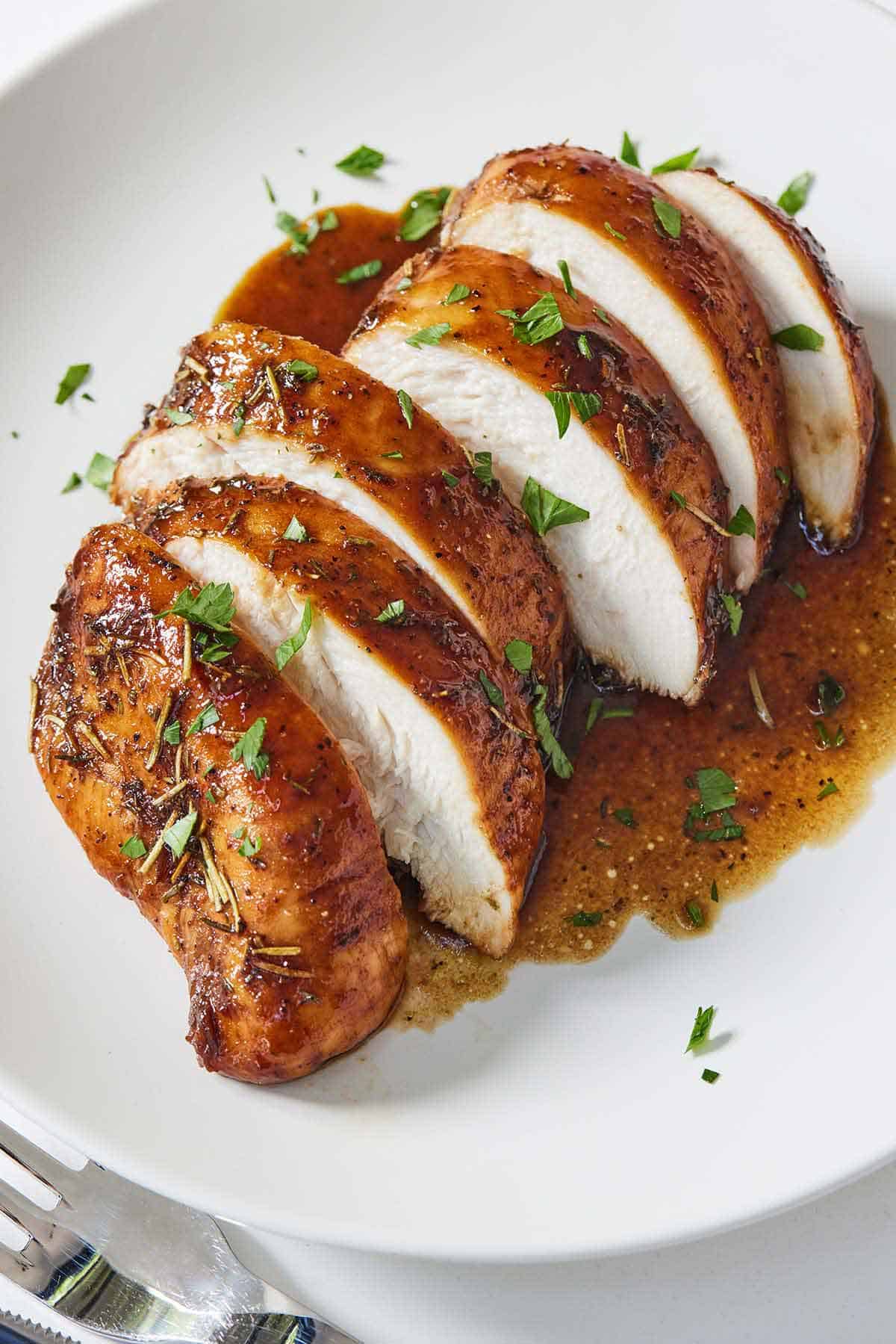 A white plate with a balsamic chicken breast, sliced.