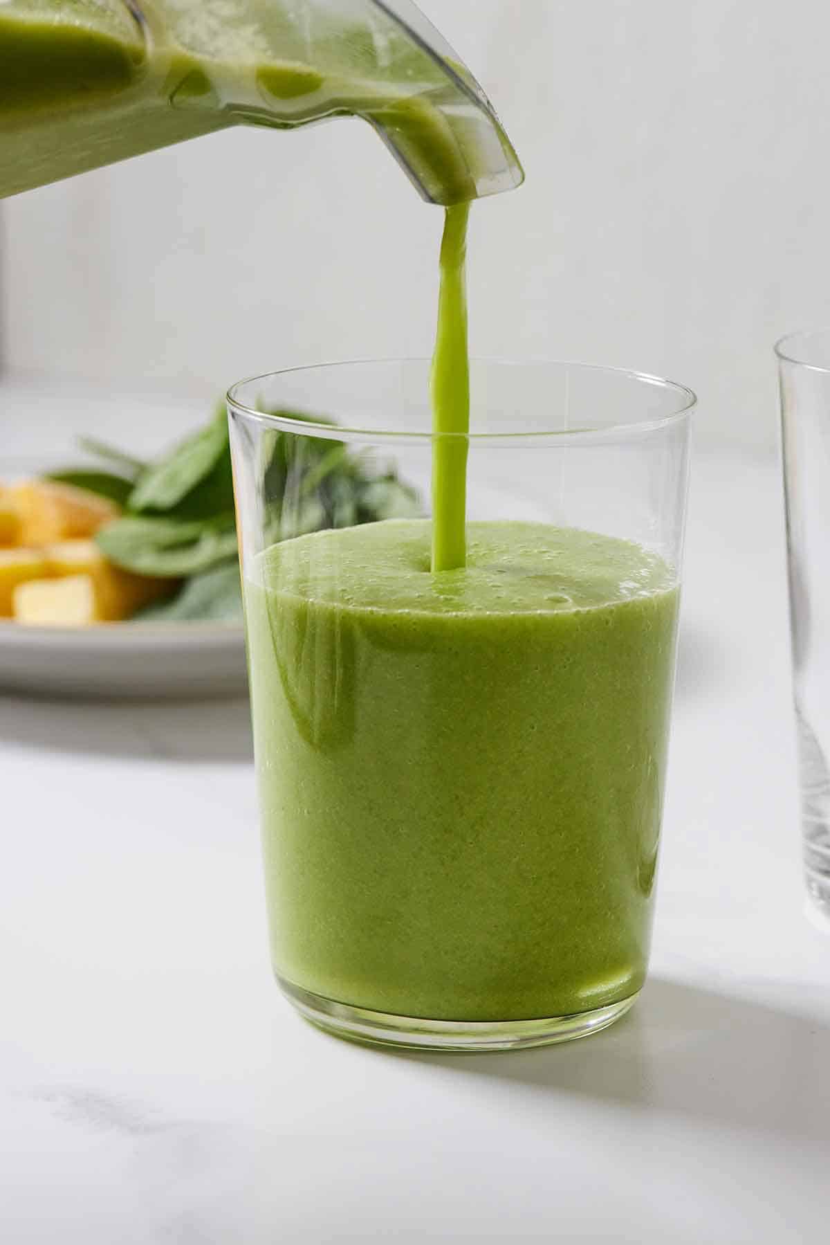 Green smoothie being poured into a glass from a blender.