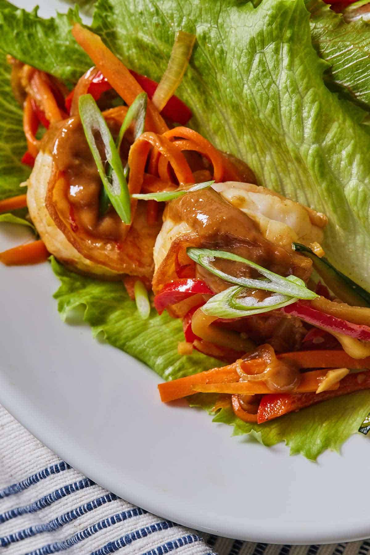 Close up of two shrimps tucked into a piece of lettuce with peanut sauce drizzled over top.