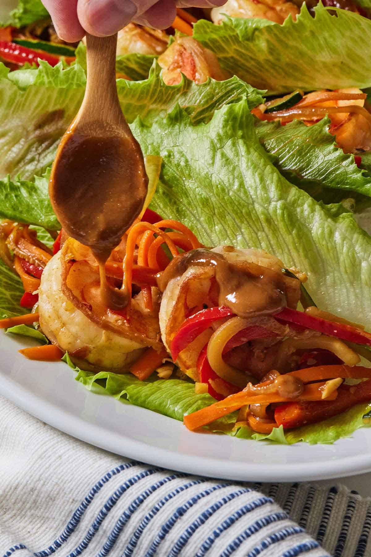 A small spoon drizzling peanut sauce over a shrimp lettuce wrap.