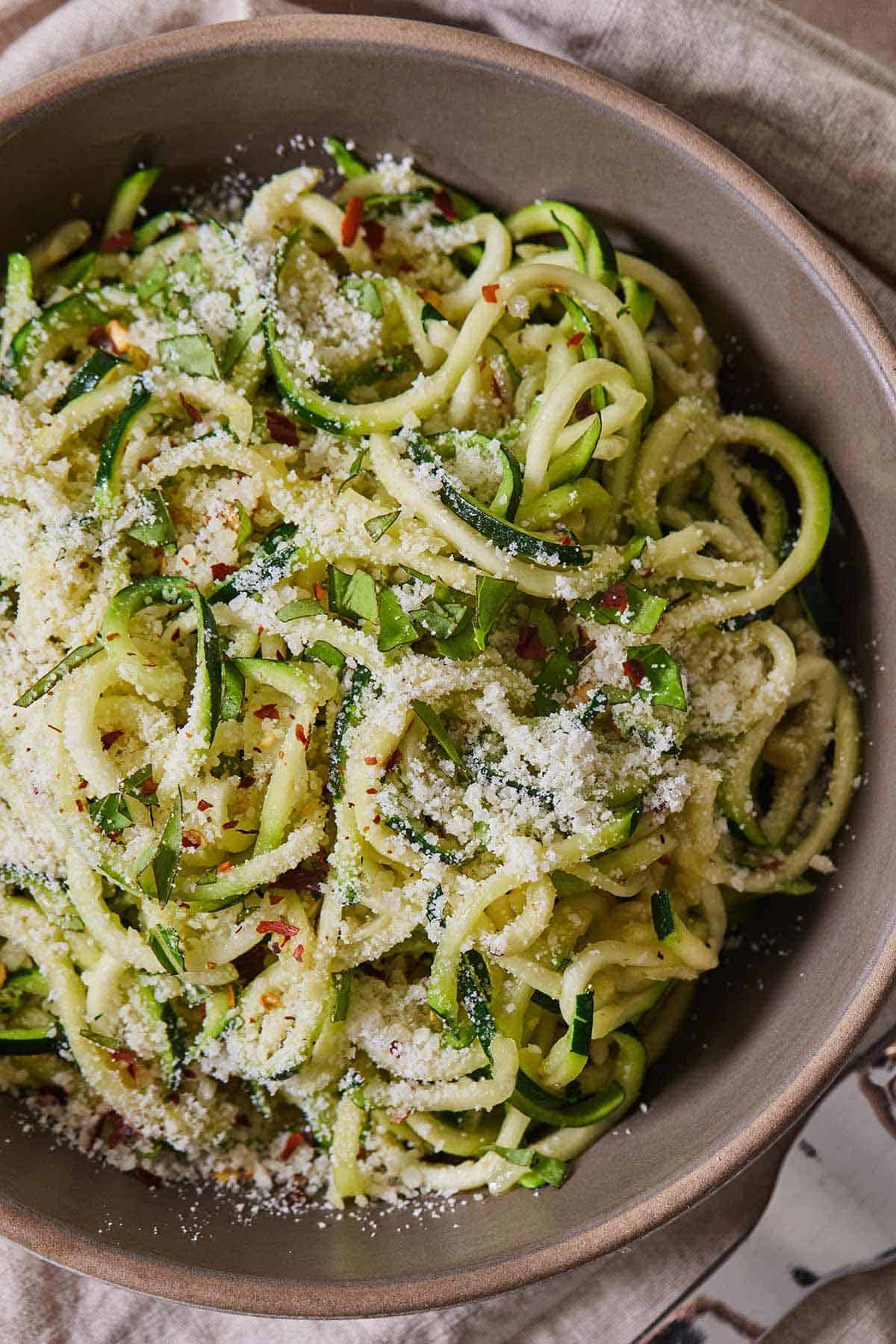 Overhead view of a bowl of zucchini noodles with parmesan and red chili flakes.