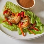 A shrimp lettuce wrap beside a pinch bowl of peanut sauce.