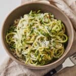 A bowl with zucchini noodles with parmesan and red chili flakes on top.