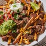 Pinterest graphic of a plate of carne asada fries with guacamole, sour cream, and cilantro.