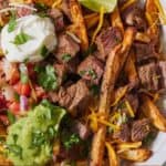 Pinterest graphic of a plate of carne asada fries with toppings and cilantro.