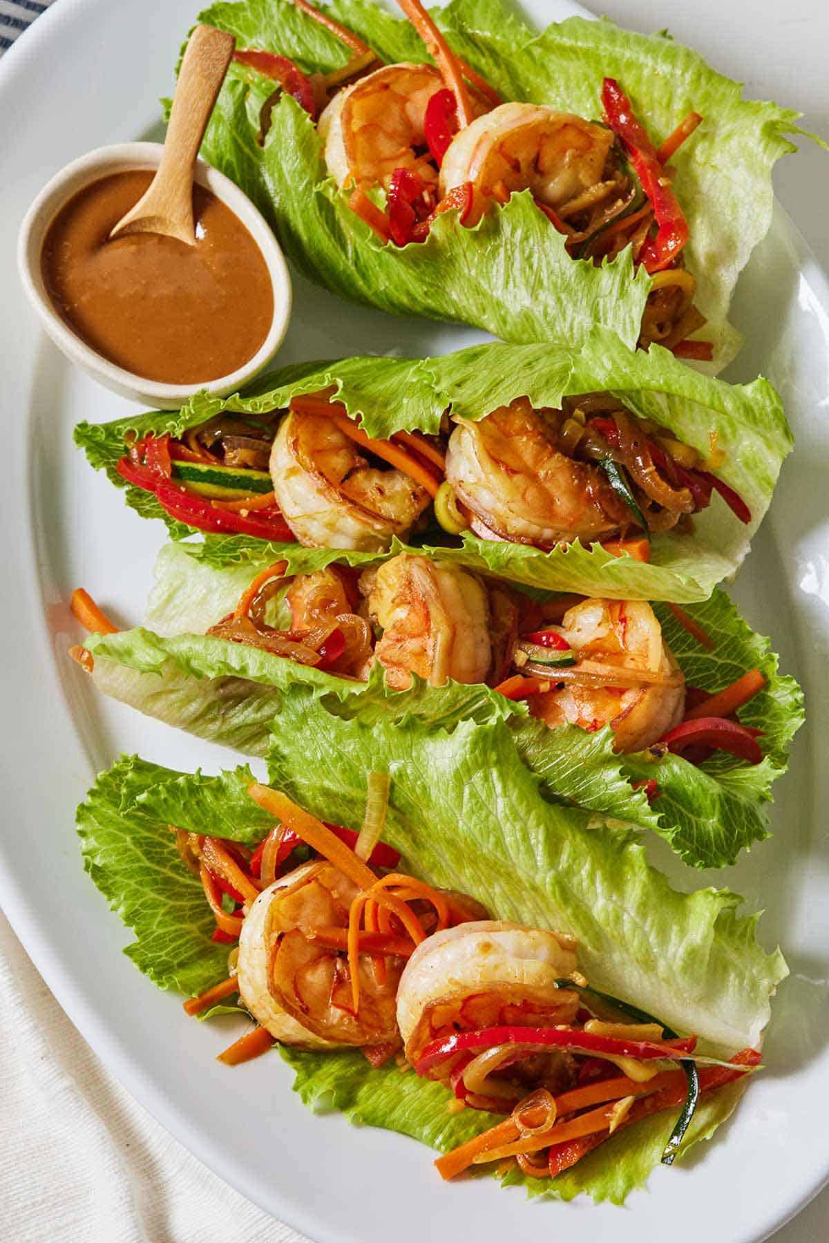 A platter with four shrimp lettuce wraps with peanut sauce on the side.